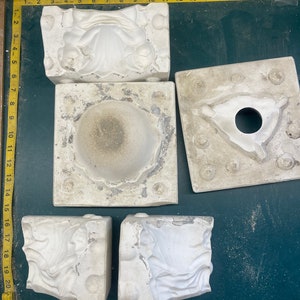 May include: Five white plaster molds for making decorative items. The molds are in various shapes, including a round bowl, a flower, and a leaf.
