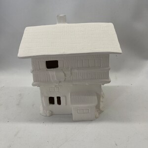 May include: White ceramic house with a gabled roof, two windows, and a chimney. The house has a rustic, cottage-style design.