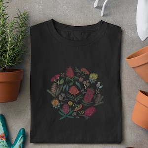 May include: Black t-shirt featuring a circular design of colourful Australian native flowers and foliage.