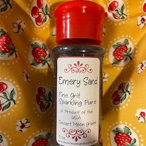 K&ouml;nnte beinhalten: Ein kleines Glas mit rotem Deckel, gef&uuml;llt mit dunkelbraunem Schmirgelsand. Das Etikett lautet "Emery Sand Fine Grit Sparkling Pure A Product of the USA Desert Moon Grains 5 oz. www.desertmoongrains.etsy.com"