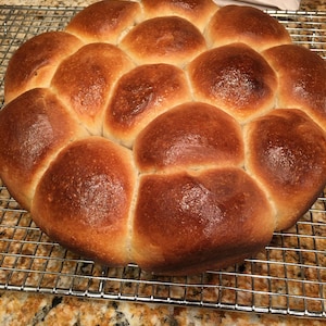 May include: A close-up of a large batch of golden brown dinner rolls on a wire rack.