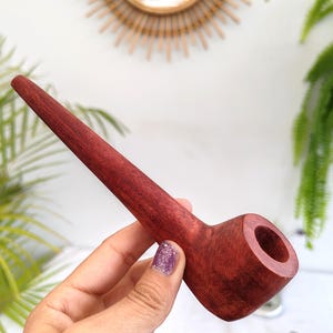 Puede incluir: Una pipa de madera de color rojo oscuro con un tallo largo y delgado y una cazoleta con una abertura redondeada.