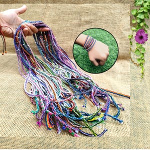 Puede incluir: Una colección de pulseras de hilo trenzado multicolor con varios patrones y pequeñas cuentas. Las pulseras se muestran en un manojo y apiladas en una muñeca, exhibiendo tonos vibrantes que incluyen azul, morado, rosa, verde y amarillo.
