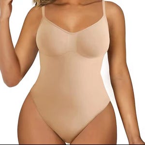 May include: A beige bodysuit with thin shoulder straps and a V-neckline. The one-piece garment has a smooth, seamless appearance and is designed to shape the torso and hips. The fabric appears to be a stretchy material.
