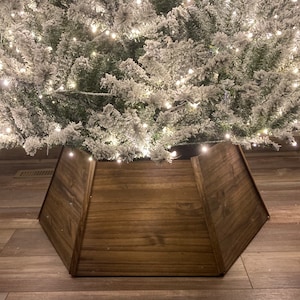 May include: A brown wooden Christmas tree skirt with a simple design. The skirt is made of three panels that meet in the center.