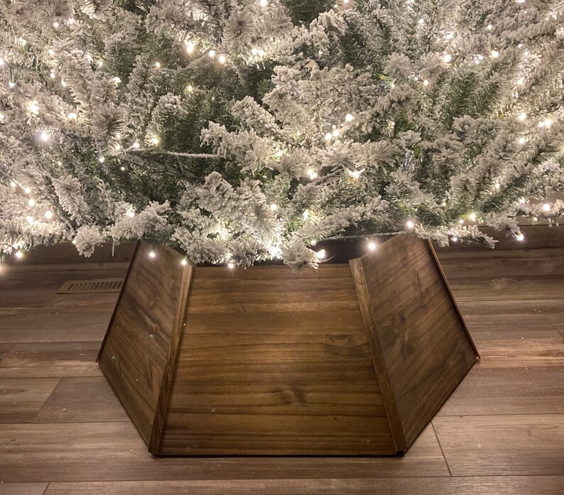 May include: A brown wooden Christmas tree skirt with a simple design. The skirt is made of three panels that meet in the center.