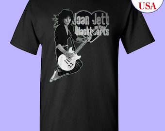 May include: Black and white image of Joan Jett and the Blackhearts on a black t-shirt. Joan Jett is playing a guitar and is jumping in the air. The band's name is in a heart shape.
