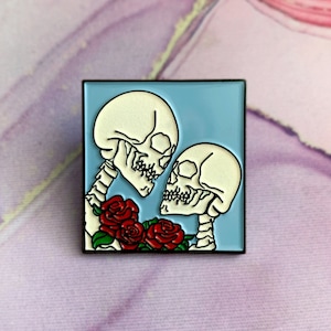 Peut inclure: Une épingle en émail bleu représentant deux squelettes qui s'embrassent avec des roses rouges. Les squelettes se font face et semblent s'embrasser.
