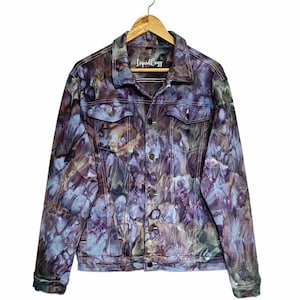 Könnte beinhalten: Eine Jeansjacke mit einem marmorierten Batikmuster in den Farben Dunkelviolett, Blau und gedecktem Braun. Die Jacke hat einen klassischen Kragen, lange Ärmel mit geknöpften Manschetten, zwei Brusttaschen mit Knopfklappen und eine Knopfleiste vorne. Der Markenname LiquidCozy ist in Weiß auf dem inneren Nackenetikett aufgedruckt.
