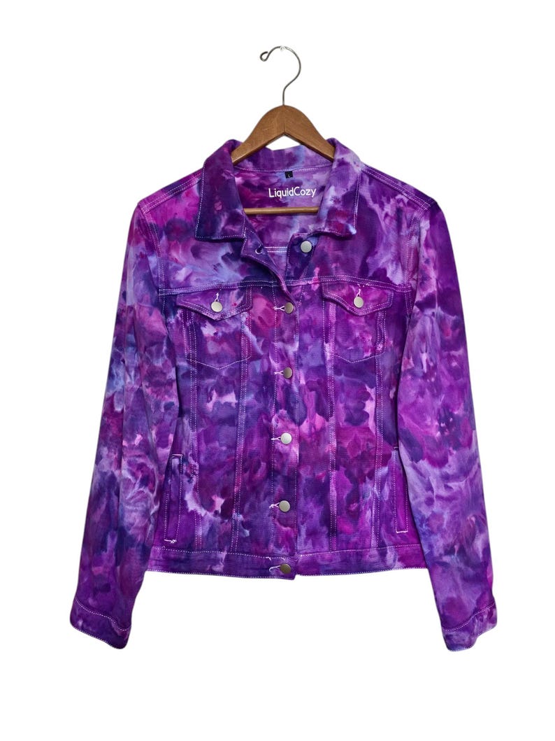 K&ouml;nnte beinhalten: Lilafarbene Batik-Jeansjacke mit einem wei&szlig;en Etikett mit der Aufschrift "LiquidCozy".