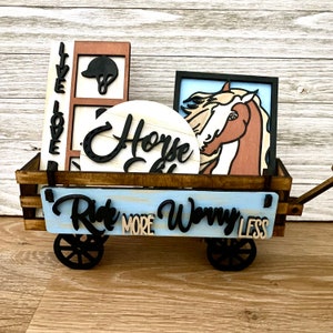 May include: A wooden wagon filled with horse-themed decorations. The wagon is painted blue and has the words "Ride More Worry Less" on the front. The decorations include a round sign that says "Horse Crazy", a sign with a horse's head, and a sign with a riding helmet.