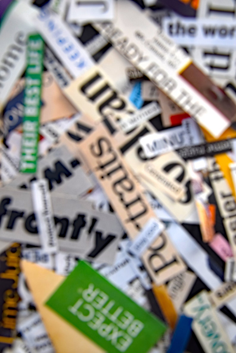 May include: A close-up of a collection of paper scraps with words like "Ready for the", "Potraits", "Expect Better", and "The World" printed on them. The scraps are arranged in a random pattern and are slightly out of focus.