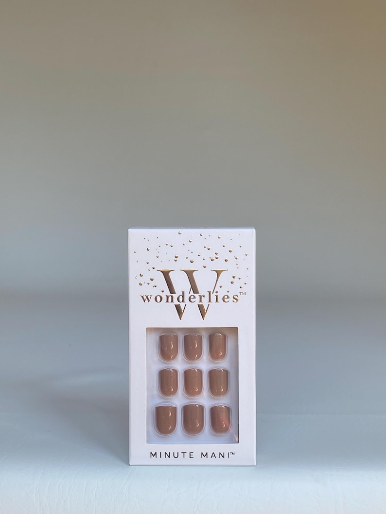 May include: A white rectangular box containing nine press-on nails in a solid tan color. The packaging features gold foil confetti accents at the top, the brand name "wonderlies" in gold lettering, and the text "MINUTE MANI" at the bottom.