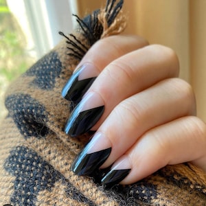 May include: Close-up of a hand with black and white nail polish. The nails are shaped into a long oval and have a black tip with a white chevron design.