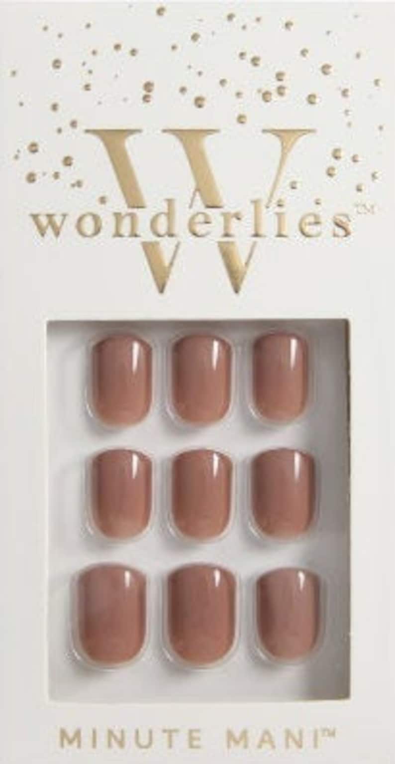 May include: A set of nine glossy, nude-colored press-on nails arranged in a three-by-three grid inside a white cardboard box. The packaging features the gold text "wonderlies" at the top and "MINUTE MANI" at the bottom with gold confetti accents.