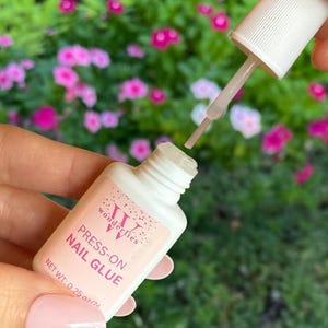 May include: A white bottle of Wonderlies press-on nail glue with a pink label. The bottle has a clear applicator with a white cap. The label says "Press-on Nail Glue" and "Net Wt. 0.25 oz/7g".