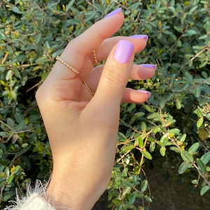 May include: A hand wearing a gold beaded ring and several other rings. The fingernails are painted a light purple color.