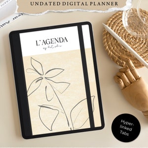 Może przedstawiać: Cyfrowy planer na tablecie z czarną okładką i beżowym tłem. Planer ma minimalistyczny design z rysunkiem rośliny i tekstem "L'AGENDA my best plan".