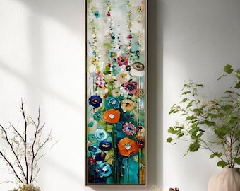 Könnte beinhalten: Ein vertikales Blumenbild mit goldenem Rahmen hängt an einer weißen Wand. Das Kunstwerk zeigt bunte Blumen in Blau-, Orange- und Rosatönen. Auf einem Holztisch sind dekorative Gegenstände ausgestellt, darunter ein Kuchen, eine Vase und eine Topfpflanze.