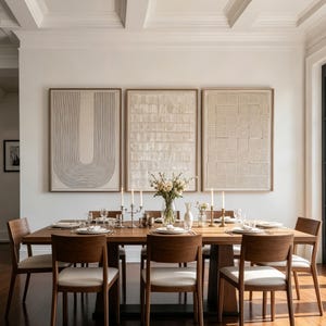 Puede incluir: Un juego de comedor con una mesa rectangular de madera y seis sillas, cada una con marco de madera oscura y asiento color crema. Tres grandes piezas de arte mural texturizado en color beige cuelgan sobre la mesa.