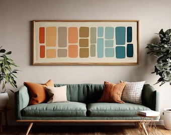 Puede incluir: Una obra de arte abstracta rectangular con marco de madera cuelga sobre un sofá verde. La obra presenta una serie de formas rectangulares coloridas en tonos naranja, marrón y azul. El sofá está adornado con cojines en tonos naranja y crema.