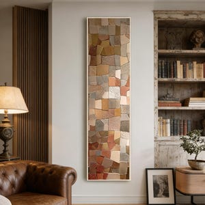 Puede incluir: Una obra de arte mural rectangular con un diseño de mosaico. El mosaico está compuesto por varias baldosas de forma irregular en tonos marrones, beige, grises y rojos. La obra de arte está enmarcada en un marco fino y de color claro y cuelga de una pared de color neutro.