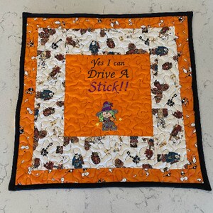 May include: Orange and white quilted square with a black border. The center features a witch with a purple hat and the text "Yes I can Drive A Stick!!".