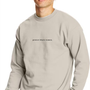 May include: A light beige sweatshirt with the text "protect black women." printed on the front.