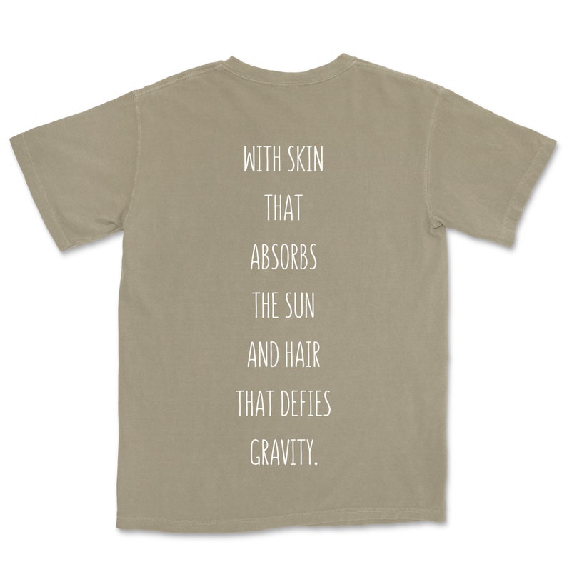May include: A light brown t-shirt with the text "WITH SKIN THAT ABSORBS THE SUN AND HAIR THAT DEFIES GRAVITY." printed on the back.