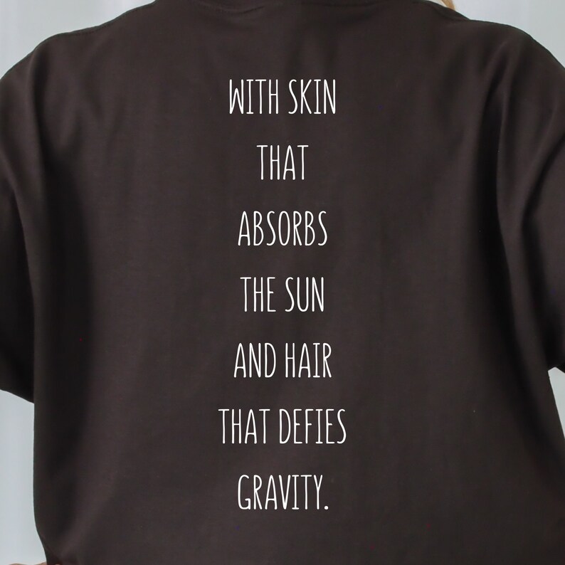 May include: Black t-shirt with white text that reads "With skin that absorbs the sun and hair that defies gravity."