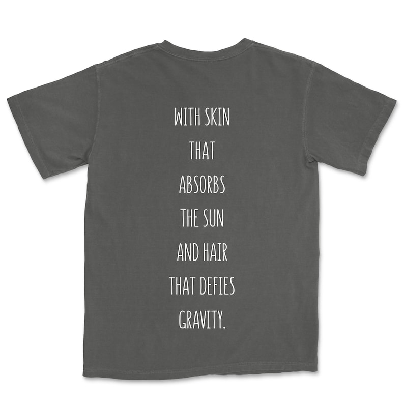 May include: A charcoal grey t-shirt with the text "WITH SKIN THAT ABSORBS THE SUN AND HAIR THAT DEFIES GRAVITY." printed on the back.