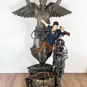 May include: A detailed statue featuring a figure in action, holding a gun, with a large angel statue in the background. The base includes a well and cage. The color palette is primarily grey, brown, and blue.