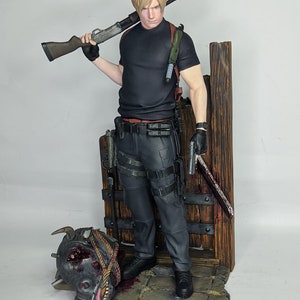 May include: A detailed figurine of a character from a video game, holding a shotgun and a pistol. The figure is dressed in black tactical clothing and stands next to a wooden structure. A monster head lies on the ground, adding to the action theme.
