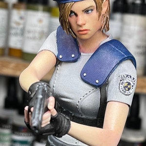 May include: A detailed figurine of a character in a blue beret and gray shirt, holding a gun. The figure has a stern expression and is wearing a tactical belt and gloves. The figure has a patch on the sleeve.