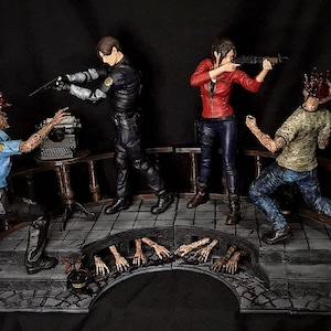 May include: A detailed diorama featuring action figures in a zombie apocalypse scene. Two figures aim weapons at zombies, while a third figure is being attacked. The figures are on a bridge with a typewriter and a table.