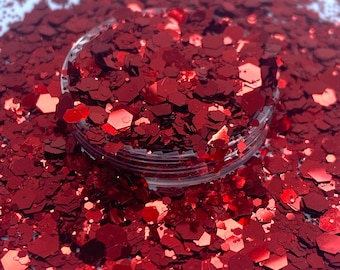 May include: A close-up of a jar filled with red glitter. The glitter is in various shapes and sizes, with a metallic sheen.