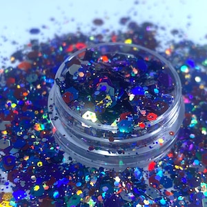 May include: A clear jar filled with iridescent glitter in shades of blue, red, green, and gold. The glitter is scattered around the jar on a white surface.