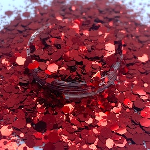 May include: A close-up of a jar filled with red glitter. The glitter is in various shapes and sizes, with a metallic sheen.