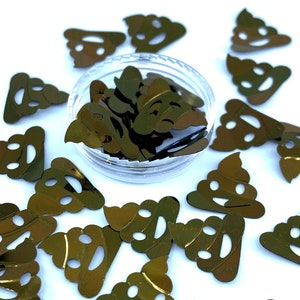 May include: Gold-colored confetti in the shape of smiling poop emojis. Some confetti is scattered around a clear plastic container filled with more of the same confetti. The background is white.
