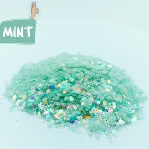 May include: A pile of mint-colored glitter with iridescent specks. The word "MINT" is in a green speech bubble in the upper left corner. A hand with the "okay" gesture is above the speech bubble.