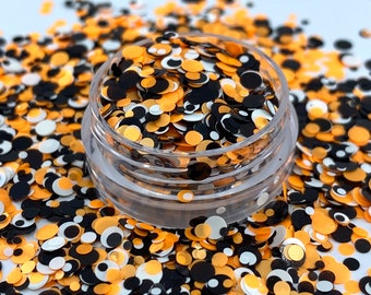 May include: A clear jar filled with orange, black, and white glitter confetti. The confetti is in the shape of circles and eyes.