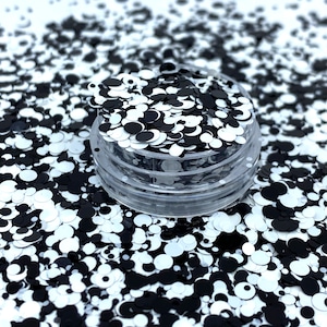 May include: A clear plastic container filled with black and white glitter. The glitter is in the shape of circles of varying sizes.