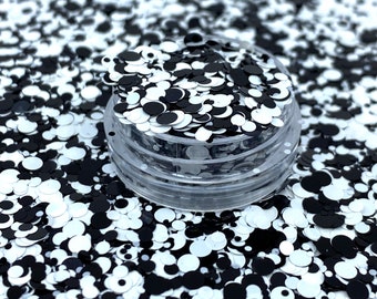 May include: A clear plastic container filled with black and white glitter. The glitter is in the shape of circles of varying sizes.