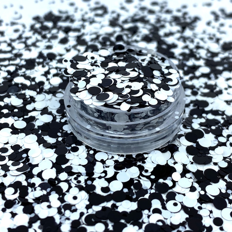 May include: A clear plastic container filled with black and white glitter. The glitter is in the shape of circles of varying sizes.
