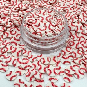 May include: White and red baseball sprinkles in a clear container. The sprinkles are small and round, with a red stitching design.