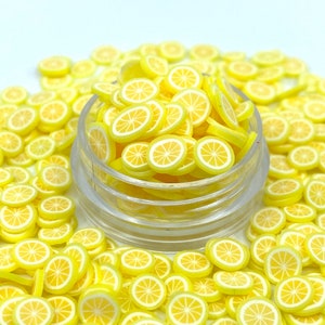 May include: A clear jar filled with yellow and white lemon slice-shaped polymer clay pieces. The miniature fruit slices are scattered around the jar, creating a bright and cheerful display. The lemon slices have a yellow rind and white flesh.