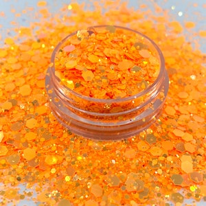 May include: A clear plastic jar filled with orange glitter. The glitter is a mix of small and large hexagons and circles.