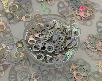 May include: A clear container filled with iridescent, silver-colored handcuff-shaped sequins. The sequins are scattered around the container, creating a shimmering effect. These decorative sequins are ideal for crafts and embellishments.