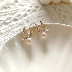 May include: A pair of gold butterfly earrings with white pearl accents. The earrings are on a white surface.