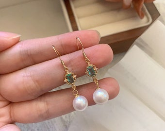 May include: Gold earrings with a green gemstone and a white pearl dangle.